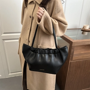 Chic black pleated cloud tote bag with gold lettering shown on model in warm office setting