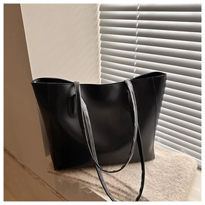 Detail of minimalist black PU leather tote bag with slim shoulder straps on a soft texture
