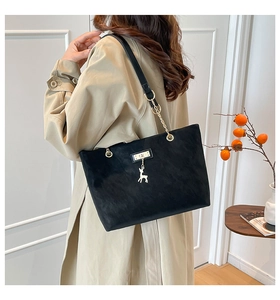 Detail of black suede tote bag featuring a gold chain strap and cute deer charm pendant