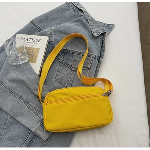 Yellow nylon crossbody bag placed on a blue denim jacket in a minimalist lifestyle setting