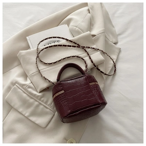 Dettaglio mini borsa bordeaux con trama a coccodrillo e tracolla a catena dorata su tessuto