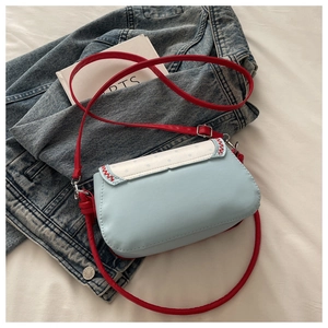 Detail of blue plaid shoulder bag with red stitching and strap on artistic backdrop