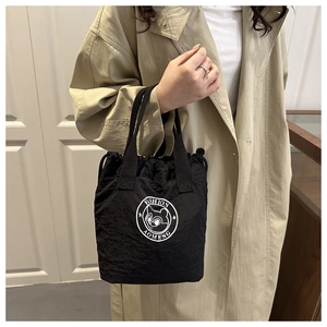 Close-up of black drawstring lunch bag with cartoon logo held by model in trench coat