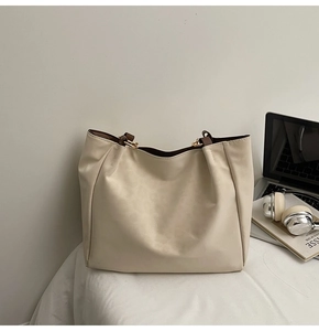 Detail of minimalist cream tote bag showing gold hardware and dark brown handles
