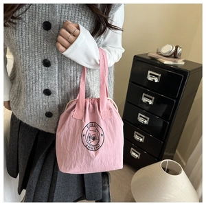 Pink drawstring bucket bag detail with squirrel logo carried by a model in a casual setting