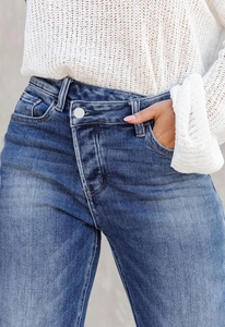 Détail de la taille haute croisée sur un jean en denim bleu avec finition délavée
