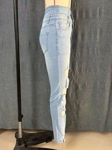 Detail of high waist light blue skinny jeans with side distressed ripped hole design