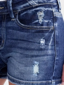 Detail shot of blue distressed denim shorts showing ripped texture and white stitching