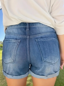 Vista posteriore di pantaloncini in denim slim con orlo risvoltato e tasche su erba