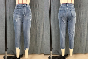 Close-up detail of distressed ripped accents and raw hem on slim-fit denim jeans