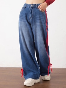 Detail of wide-leg blue jeans with side red stripes and bow ribbon ties at the hem