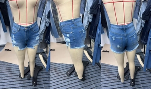 Close-up of distressed denim shorts with heavy ripped details and frayed raw hem