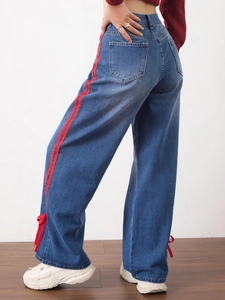 High-waisted wide-leg dark blue jeans with red side stripes and ankle bow details