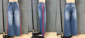 Detail of dark blue wide leg jeans featuring red side ribbons and delicate leg bows