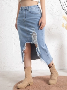 Detail of distressed light blue denim skirt featuring ripped holes and raw frayed hemline