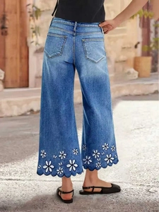 Back view of women's wide leg denim jeans with daisy embroidery and wavy cutout hem