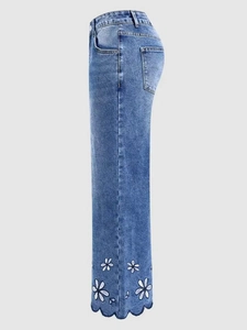 Detailed view of white floral embroidery and scalloped hem on blue denim cropped jeans