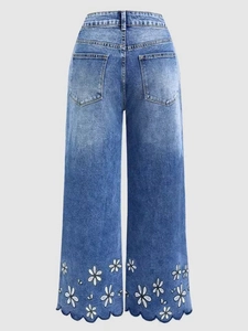 Detail of white daisy embroidery and scalloped cutout edges on blue denim jeans