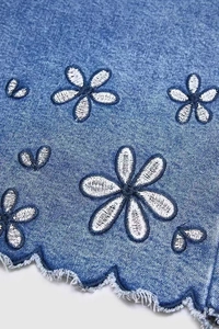 Detail of white daisy embroidery on blue denim with scalloped raw hem and frayed edges