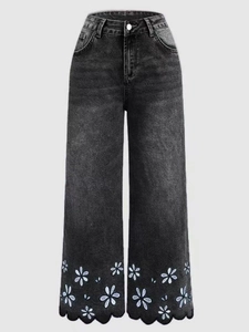Close-up of white daisy embroidery and scallop wave edges on washed grey denim jeans