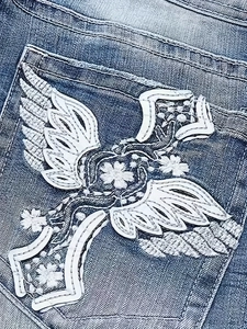 Blue wash jeans featuring large white embroidered cross and wings on the back pocket