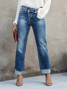 Détail d'un jean taille haute bleu avec taille croisée et revers à franges sur le bas