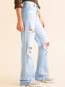Détail d'un jean bleu clair taille haute avec déchirures aux genoux et jambes larges droites
