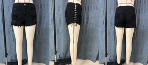 Detailed view of black denim shorts with side lace-up eyelets and distressed frayed hem