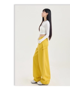 Détail latéral d'un pantalon cargo jaune ample avec broderie de lettres orange