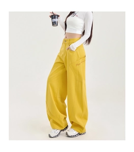 Gros plan du pantalon cargo jaune avec broderie de lettres rouges sur les poches latérales