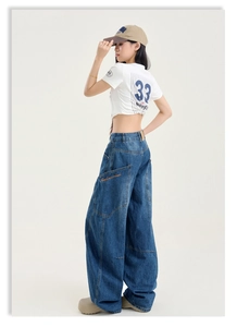 Détail d'un jean cargo large avec broderie de lettres oranges sur la poche latérale
