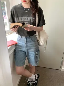 Detail of high-waist cargo denim shorts and grey graphic tee on a girl by a window
