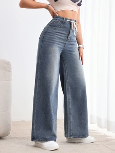 Détail d'un jean taille haute à jambes larges avec cordon de serrage et denim délavé
