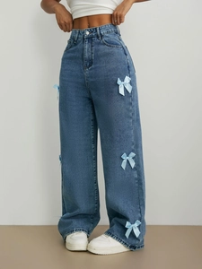 Détail de nœuds en ruban bleu clair sur un jean droit délavé montrant la texture coton
