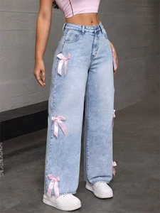 Détail de jean bleu clair à jambes larges avec des nœuds décoratifs en soie rose sur les côtés