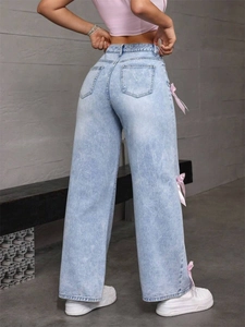 Détail d'un jean taille haute à jambe large avec trois nœuds en satin rose sur le côté