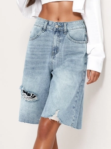 Detail view of frayed hem and distressed ripped holes on light blue denim shorts