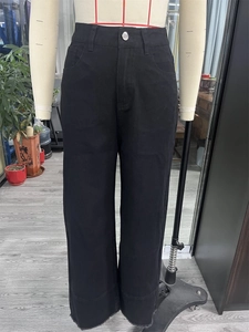 Detail of high waist black denim wide leg jeans with metal button and raw hem fringe