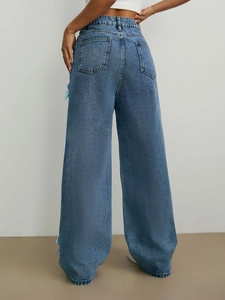 Détail d'un jean bleu à taille haute et jambe large avec des nœuds en soie sur le côté
