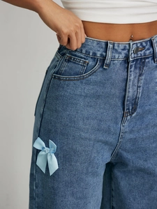 Détail d'un jean large en denim bleu avec un nœud en ruban bleu clair sur la poche
