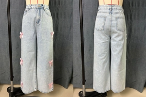 Détail d'un jean bleu clair à jambes larges avec des nœuds en satin rose sur les côtés style ballet