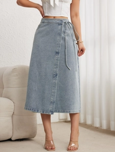 Détail d'une jupe mi-longue portefeuille en denim bleu clair avec nouage à la taille