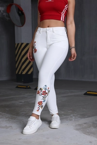 Détail de broderie florale colorée sur un jean blanc taille haute coupe slim pour femme