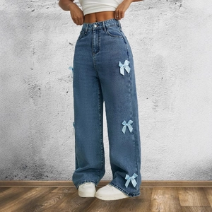 Dettaglio dei jeans blu a vita alta con gamba larga e fiocchi decorativi in seta laterali
