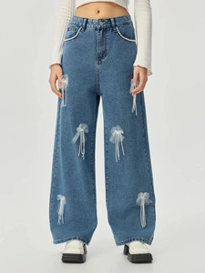 Detailansicht der weiten Blue Jeans mit weißen Netzschleifen und Perlenquasten-Dekor