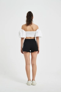 Rear view of model wearing white off-shoulder puff sleeve top and black denim shorts