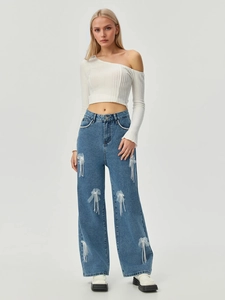 Detailansicht der weiten Jeans mit weißen Mesh-Schleifen und Perlenquasten-Fransen