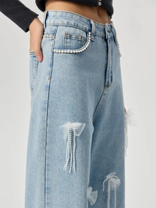 Detail der hellblauen Jeans mit Mesh-Schleifen und hängenden Perlenfransen-Akzenten