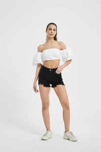 Detail of black denim shorts with raw hem paired with a white off-shoulder puff sleeve top
