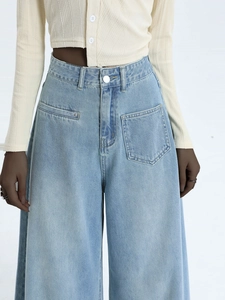 Detail view of high-waisted wide-leg denim jeans in light blue wash with asymmetrical pockets